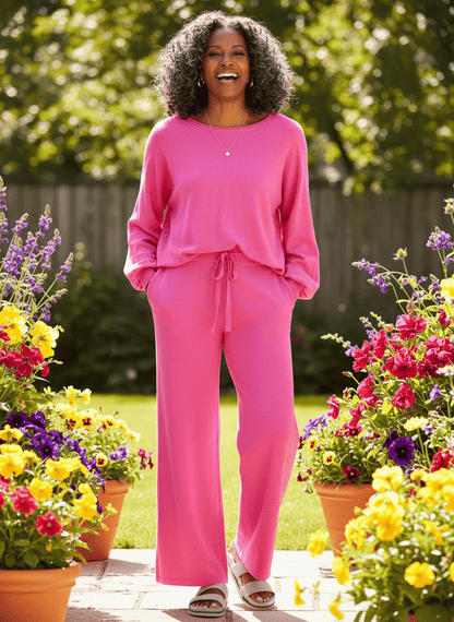 Smiling woman in pink Comfee lounge set standing in garden with colorful flowers